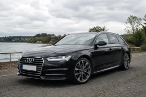 Black Audi A6 Avant parked beside a lake, photographed from the front three-quarter angle.
