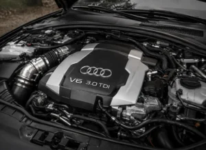 Close-up view of an Audi V6 3.0 TDI engine bay with engine cover, intake system, hoses and mechanical components.